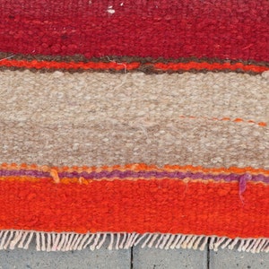 May include: A colorful striped rug with a fringe border. The rug has red, orange, brown, beige, and purple stripes.