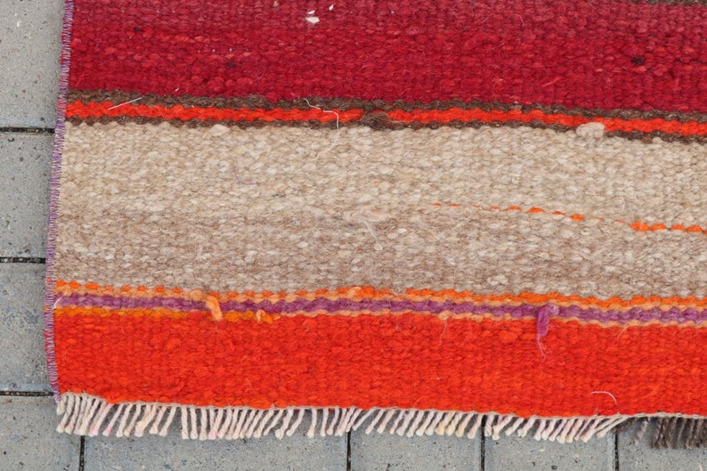 May include: A colorful striped rug with a fringe border. The rug has red, orange, brown, beige, and purple stripes.