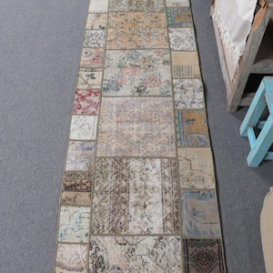 May include: A long, rectangular patchwork rug with a variety of colors and patterns. The rug is made up of smaller squares and rectangles of different fabrics, including floral patterns, geometric designs, and solid colors. The rug is primarily beige and brown with accents of red, blue, and green.