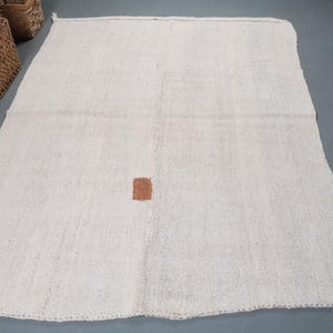 May include: A white woven rug with a small brown patch in the center.