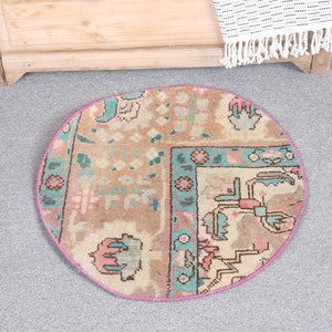 May include: A round, cream-colored rug with a pink border and a colorful floral pattern. The rug has a traditional design with turquoise, pink, and cream colors.