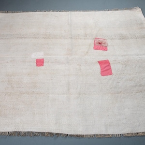 Puede incluir: Una alfombra blanca con una textura tejida sutil y tres parches rosas cosidos.