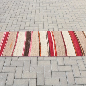 May include: A long, narrow, striped rug with red, orange, brown, and white stripes. The rug is made of a woven material and has a rustic, hand-crafted look.