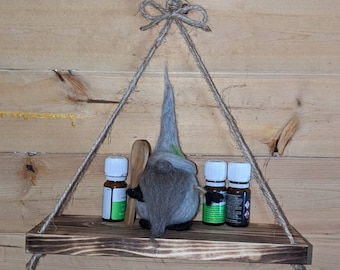 May include: A wooden shelf with a gnome figurine and three bottles hanging from a rope. The shelf is stained dark brown and has a rustic look. The gnome is grey and has a long white beard. The bottles are clear glass with white caps and green liquid inside.