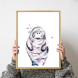 May include: A watercolor painting of a manatee with a light purple and blue color scheme. The manatee is surrounded by small blue circles, resembling bubbles.