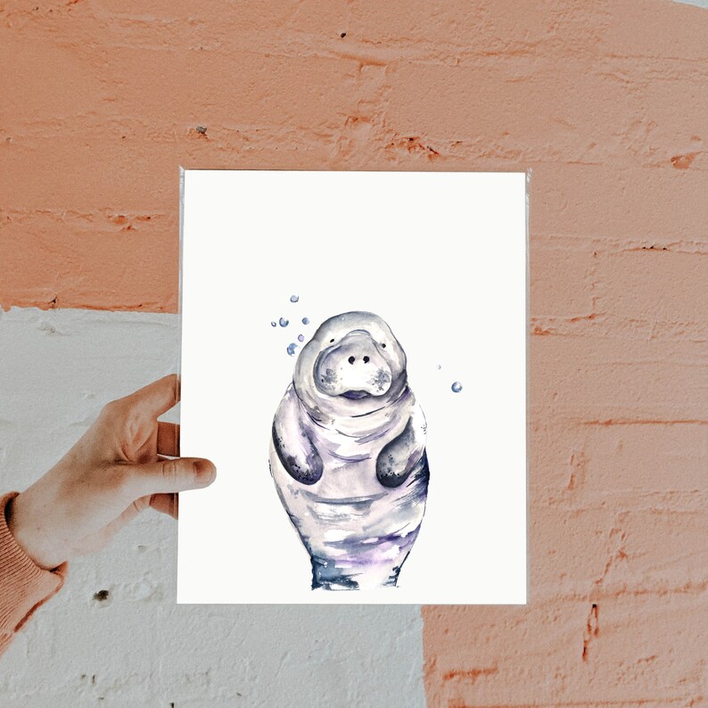 May include: A watercolor painting of a manatee with a light blue, purple, and gray color scheme. The manatee is depicted with a friendly expression and is surrounded by small blue dots, suggesting bubbles.