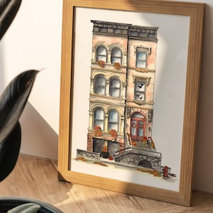 May include: A framed watercolor illustration of a three-story brick building with a brown door and a stone stoop. The building has a pink facade and windows with white trim. There are pumpkins and fall leaves on the stoop.