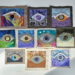 May include: A collection of ten fabric patches featuring embroidered eye designs. Each square or rectangular patch displays a unique eye motif with stitched eyelashes, colorful patterned fabric backgrounds, and varied textures in shades of blue, purple, green, and orange.
