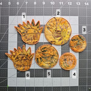May include: Six embroidered patches with a yellow and orange color scheme. The patches feature a cartoon-like creature with a crown and a toothy grin. The patches are numbered 1 through 6.