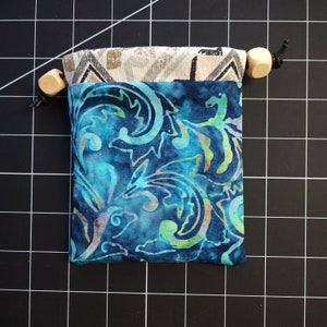 May include: A small blue drawstring bag with a floral pattern. The bag has a white lining and wooden toggles.