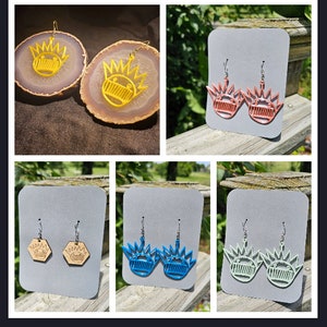 May include: A set of six pairs of earrings featuring a cartoon character with a crown. The earrings are made of different materials, including wood, metal, and plastic. The earrings are available in a variety of colors, including yellow, pink, blue, and green.
