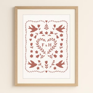 Peut inclure: Impression encadrée avec un motif terracotta sur fond blanc. Le motif comprend des oiseaux, des fleurs, des cœurs et les lettres "F & H" dans une couronne en forme de cœur. L'impression est dans un cadre en bois brun clair.
