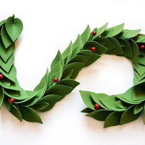May include: A green felt garland with red felt berries. The garland is made of individual felt leaves that are sewn together. The garland is in the shape of a circle.