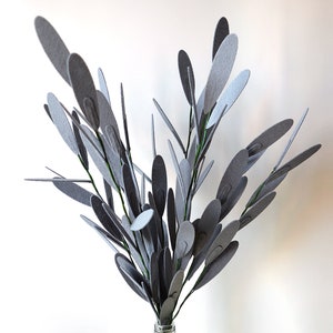 Puede incluir: Un ramo de hojas de fieltro gris dispuestas en un jarrón. Las hojas son de diferentes tamaños y formas, y están agrupadas para crear un aspecto lleno y exuberante.