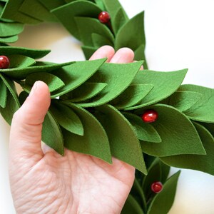 May include: A green felt garland with red felt berries. The garland is made of individual felt leaves that are layered to create a 3D effect.