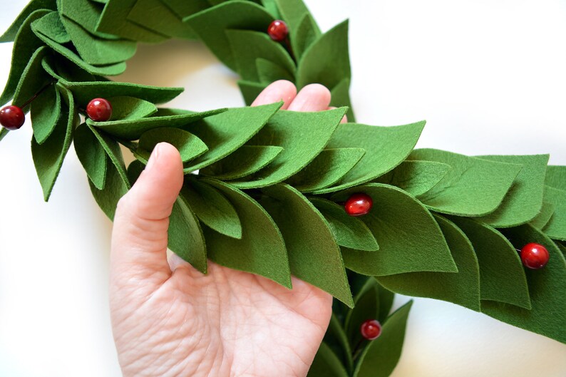 May include: A green felt garland with red felt berries. The garland is made of individual felt leaves that are layered to create a 3D effect.
