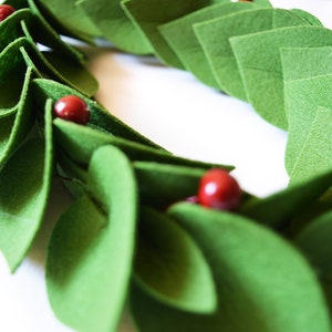 May include: A green felt wreath with red felt berries. The wreath is made of individual felt leaves that are sewn together.