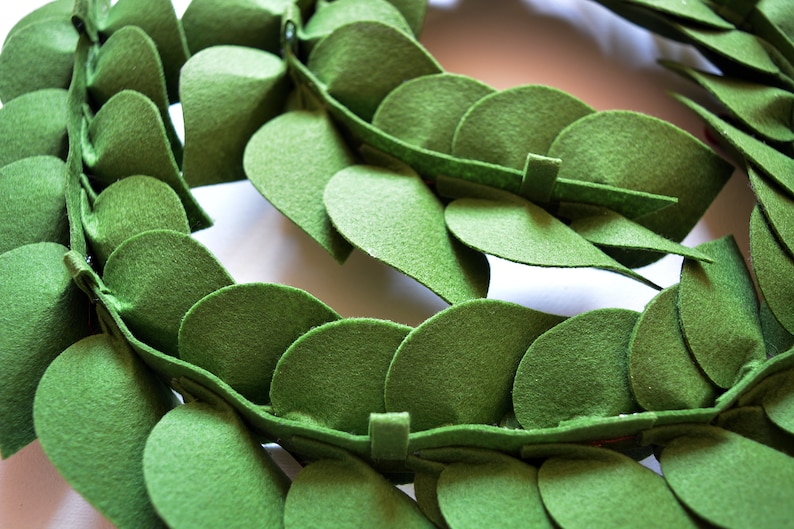 May include: A close-up of a green felt garland made of individual leaves. The leaves are sewn together to create a continuous garland.