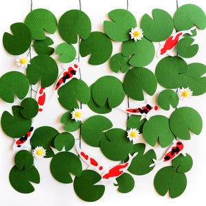 May include: A decorative wall hanging featuring green lily pads, white flowers, and koi fish with red and black markings. The arrangement is set against a white background, creating a serene, nature-inspired aesthetic.