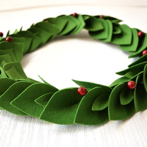 May include: A green felt wreath with red felt berries. The wreath is made of individual felt leaves that are layered to create a full and lush look.
