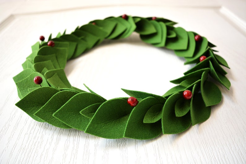 May include: A green felt wreath with red felt berries. The wreath is made of individual felt leaves that are layered to create a full and lush look.