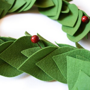 May include: A green felt garland with red berries. The garland is made of individual felt leaves that are sewn together.