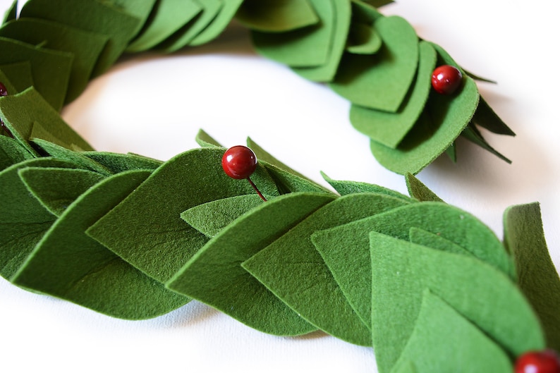 May include: A green felt garland with red berries. The garland is made of individual felt leaves that are sewn together.