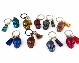 May include: A collection of ten skull keychains, each featuring a small resin skull in various colors including blue, gold, red, grey, and pink. Each keychain includes a metal ring and a matching or coordinating faux leather tassel.