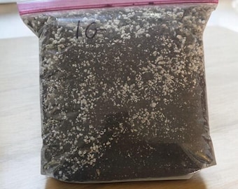 May include: A clear plastic bag with a pink zipper closure contains a dark gray and white mixture. The bag is labeled with the number "16".