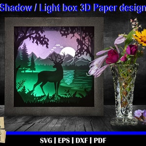 Könnte beinhalten: Ein 3D-Papierbastel-Design eines Hirsches, der in einer Waldszene mit einem Vollmond im Hintergrund steht. Das Design befindet sich in einem Schattenkastenrahmen mit einem grün-lila-blauen Farbschema. Das Design ist für eine Lichtbox und ist in den Formaten SVG, EPS, DXF und PDF verfügbar.