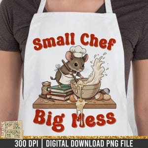 May include: White apron with a cartoon illustration of a mouse chef mixing batter in a bowl. The text "Small Chef Big Mess" is in red. The image includes eggs, a whisk, and a stack of books.