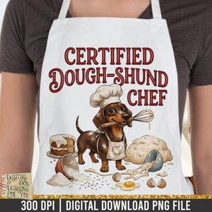 May include: White apron with a cartoon dachshund chef holding a whisk and wearing a chef's hat. The apron has the text "CERTIFIED DOUGH-SHUND CHEF" in maroon. Baking ingredients and a cake are also illustrated on the apron.