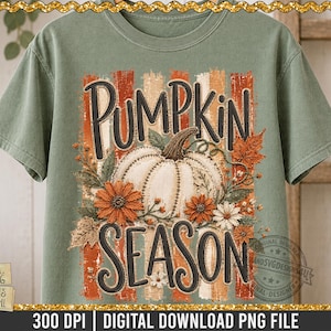 Peut inclure: Un t-shirt vert sauge avec une impression graphique portant le texte PUMPKIN SEASON en lettres noires. Le motif comprend une citrouille blanche centrale, des fleurs orange et blanches, des feuilles d'automne et des rayures verticales.
