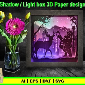 Puede incluir: Un diseño de papel 3D con Santa Claus sosteniendo una linterna y un ciervo de pie en una escena de pueblo nevado. El diseño está iluminado con luces moradas, rosas y azules. El diseño está etiquetado como "Shadow / Light box 3D Paper design".