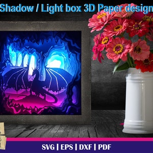 May include: A 3D papercraft design of a dragon emerging from a cave. The design is lit from behind, creating a colorful glow. The design is framed in a black frame and is ready to be assembled.