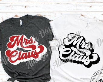 Op de afbeelding: Twee T-shirts met de tekst "Mrs. Claus" in een retro-lettertype. Het T-shirt links is donkergrijs met rode tekst. Het T-shirt rechts is wit met zwarte tekst. Beide T-shirts hebben de tekst "Always Earth Day" in de rechterbenedenhoek.