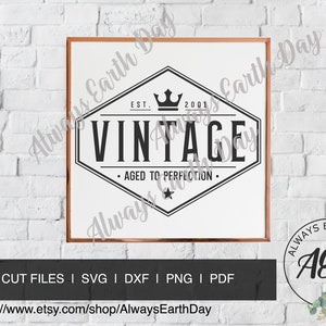 May include: A black and white vintage logo design with a crown and star. The logo says "EST. 2001 VINTAGE AGED TO PERFECTION." The logo is displayed in a white frame with a copper colored border.