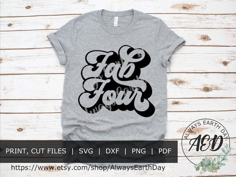 May include: A gray t-shirt with a black graphic that says "Fab Four" in a retro font style. The shirt is on a white wood background.