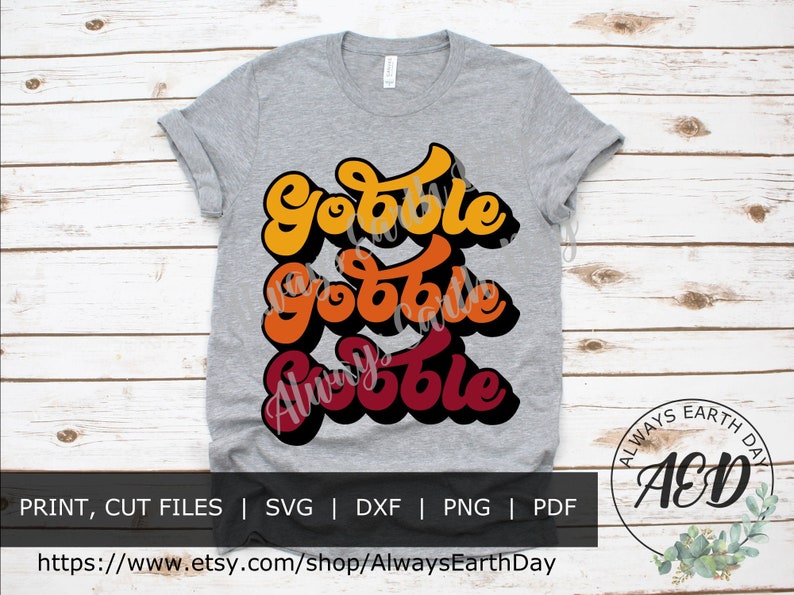 May include: A gray t-shirt with a layered design of the word "Gobble" in three different shades of orange, red, and yellow. The text is in a retro, 70s style font. The shirt is a great design for Thanksgiving.
