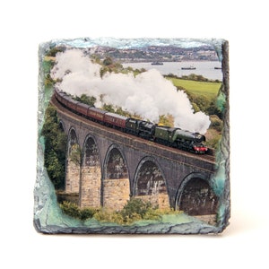 Peut inclure: Sous-verre en ardoise rectangulaire représentant un train à vapeur traversant un pont en arc de pierre. Le train est vert foncé et rouge, avec de la vapeur blanche. Le fond montre un paysage côtier.