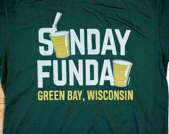 Könnte beinhalten: Ein dunkelgrünes T-Shirt mit dem Text "SUNDAY FUNDAY GREEN BAY, WISCONSIN" in weißen Buchstaben. Das Shirt zeigt zwei gelbe Plastikbecher mit Strohhalmen.