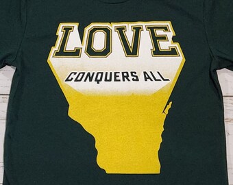Könnte beinhalten: Ein dunkelgrünes T-Shirt mit einem gelben und weißen Grafikdruck des Bundesstaates Wisconsin. Die Grafik lautet "LOVE CONQUERS ALL" in einer fetten, weißen Schrift.