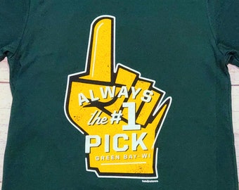 Könnte beinhalten: Grünes T-Shirt mit einer gelben Hand, die die Nummer eins zeigt. Der Text auf dem Shirt lautet "Always the #1 Pick Green Bay, WI".