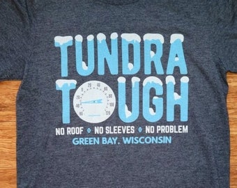 Könnte beinhalten: Ein dunkel-melierter grauer T-Shirt mit einem blauen und weißen Grafikdesign. Die Grafik zeigt den Text "Tundra Tough" mit einem Thermometer und den Text "Kein Dach, keine Ärmel, kein Problem. Green Bay, Wisconsin."