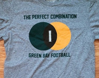 Könnte beinhalten: Ein graues T-Shirt mit einer grünen und gelben Grafik eines Fußballs und dem Text "The Perfect Combination Green Bay Football".
