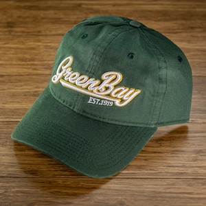 May include: A green baseball cap with white and yellow embroidered text that reads "Green Bay EST. 1919".