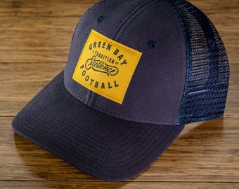 Könnte beinhalten: Eine marineblaue und gelbe Baseballkappe mit Netzrücken. Die Vorderseite der Kappe hat einen gelben Patch mit dem Text "Green Bay A Tradition of Excellence Football".