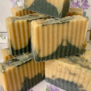 May include: A stack of handmade soap bars with a layered design. The soap features a light beige top and a dark gray base, with a wavy transition between the colors. The bars have a textured, ridged surface.