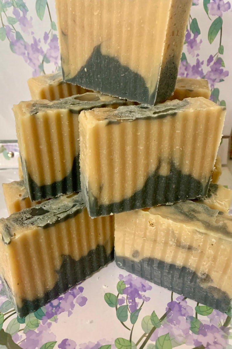May include: A stack of handmade soap bars with a layered design. The soap features a light beige top and a dark gray base, with a wavy transition between the colors. The bars have a textured, ridged surface.