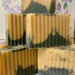 May include: A stack of handmade soap bars with a two-tone design. The top portion is a light beige, while the bottom features a dark, swirled pattern. The bars have a textured, ridged surface. The background has a floral pattern.
